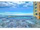 Condo beachfront pool with ocean views, brick pavers, and several lounge chairs beneath a partly cloudy, blue sky at 18610 Gulf Blvd # 607, Indian Shores, FL 33785