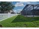 Spacious backyard with lush green grass, a white picket fence, and a screened-in pool area at 10513 Palm Cove Ave, Tampa, FL 33647