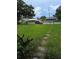 View of a front yard with overgrown grass, a walkway, and neighborhood houses at 3614 E Grove St, Tampa, FL 33610