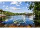 Scenic lake view featuring a dock with gazebo, boat house and lily pads under a blue sky with scattered clouds at 16205 Sentry Woods Ct, Odessa, FL 33556
