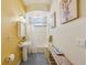 Yellow bathroom with a pedestal sink, tiled shower/tub, and a wooden bench with toiletries at 6543 Louise Ct, Hudson, FL 34667