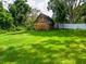 Lush green backyard featuring a rustic wooden shed, surrounded by well-maintained grass and a white fence at 7211 Red Oak Loop, New Port Richey, FL 34654