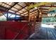 Red wooden stalls inside barn with metal roof and storage areas, ideal for equestrian needs and outdoor activities at 408 River Bed Ct, Wimauma, FL 33598