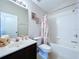 A well-lit bathroom showcasing a single sink vanity, toilet, and a shower-tub combination with patterned curtain at 4116 Knollpoint Dr, Wesley Chapel, FL 33544