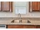 A stainless steel double sink and window are surrounded by dark wood cabinets and granite countertops at 11541 Tangle Branch Ln, Gibsonton, FL 33534