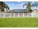 Backyard featuring lush green grass, white picket fence and an enclosed pool with palm trees at 31244 Baclan Dr, Wesley Chapel, FL 33545