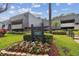 Condominium building featuring a well-maintained lawn, colorful flower beds, and a community sign at 36750 Us 19 N # 09208, Palm Harbor, FL 34684