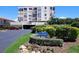 Exterior shot of a white condo building with balconies, lush landscaping, and a community sign at 6218 Palma Del Mar S Blvd # 503, St Petersburg, FL 33715