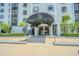 Building entrance with covered canopy, palm trees, and manicured shrubs at 14820 Rue De Bayonne # 301, Clearwater, FL 33762