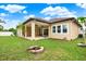 View of rear exterior with covered patio, expansive lawn area and fire pit under a cloudy blue sky at 17838 Morninghigh Dr, Lutz, FL 33549