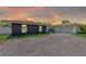 Single-story home at sunset featuring a stone facade, two-car garage, and spacious driveway leading up to the house at 9027 Merrimoor Blvd, Seminole, FL 33777