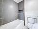 Bathroom showing a white bathtub with gray tiled walls and a built-in shelf, next to a toilet with storage at 1011 Newton S Ave, St Petersburg, FL 33705