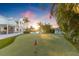 Backyard putting green with synthetic grass, palm trees, and a view of the outdoor kitchen and pool area at sunset at 511 Windward Psge, Clearwater Beach, FL 33767