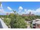 The view showcases a historic pink hotel amid palm trees, other lush trees and partly cloudy skies at 700 Beach Ne Dr # 606, St Petersburg, FL 33701