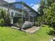 View of the screened in pool enclosure in the backyard with green grass and lush plants at 1247 Gentilly Ln, Wesley Chapel, FL 33544