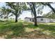 View of the home's exterior with lush green grass, mature trees and bright blue skies at 1008 Shangri La Dr, Seffner, FL 33584