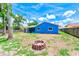 View of the backyard with a fire pit and shed, framed by a vibrant blue house and a clear sky at 2063 De Carlo Ave, Spring Hill, FL 34608
