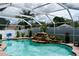 Screened-in pool featuring a rock waterfall and tropical landscaping with view of surrounding homes at 28826 Windover St, Wesley Chapel, FL 33545