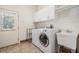 Well-lit laundry room with white washer and dryer, utility sink, storage cabinets, and a shelving unit at 4710 Troydale Rd, Tampa, FL 33615