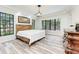 Bedroom with gray washed wood flooring, wooden bed frame, and views to outdoor greenery at 7803 Mathern Ct, Lakewood Ranch, FL 34202
