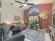 Cozy living room featuring a vaulted ceiling, brick accent wall, and large arched window with garden views at 18930 Wood Sage Dr, Tampa, FL 33647