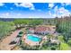 Aerial view of community pool, surrounding buildings, parking area and lush trees under a bright blue sky at 4407 Whitton Way, New Port Richey, FL 34653