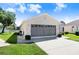 View of single-story home's garage with gray garage door, well-kept lawn, and lake views at 4407 Whitton Way, New Port Richey, FL 34653