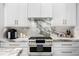 Close-up of a modern stove with marble backsplash and countertops, complemented by white cabinets and gold hardware at 10003 Brompton Dr, Tampa, FL 33626