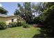 Large backyard with a lush lawn, mature trees, a pergola, and a glimpse of the yellow home at 13637 13Th St, Dade City, FL 33525