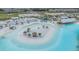 Aerial view of a white sand lagoon-style community pool with beach umbrellas, bar, and lounge area at 10278 Otter Sky Ct, San Antonio, FL 33576