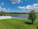 Lush backyard featuring green grass, a young tree, and a white fence overlooking a peaceful lake at 12931 Twin Bridges Dr, Riverview, FL 33579