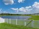 Idyllic backyard view featuring a white fence bordering a serene lake under a bright, partly cloudy sky at 12931 Twin Bridges Dr, Riverview, FL 33579