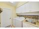 This laundry room features white cabinets, a granite countertop, a stainless steel sink, and stylish tile backsplash at 6250 Fairskies Dr, New Port Richey, FL 34655