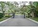 Community entrance with black metal gate and mature trees lining the driveway at 11501 Cerca Del Rio Pl, Temple Terrace, FL 33617
