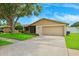 Charming single-story home with a lush green lawn, mature tree, and a neutral-toned exterior with attached garage at 12156 Meadowbrook Ln, Largo, FL 33774