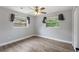 Cozy bedroom features wood-look floors, a ceiling fan, and two bright windows with greenery views at 1586 Linwood Dr, Clearwater, FL 33755