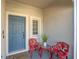 Cozy front porch featuring a welcome mat, two red chairs, a side table and blue front door at 7124 Summer Holly Pl, Riverview, FL 33578