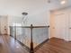 Hallway featuring hardwood floors, decorative railing, and a stylish chandelier at 7700 Bronze Oak Dr, Wesley Chapel, FL 33545