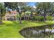 Scenic backyard view featuring a lush lawn, mature trees, a black fence, and a tranquil pond at 8358 Dunham Station Dr, Tampa, FL 33647