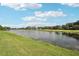 Scenic lake view with lush green grass, trees, and blue skies, creating a peaceful and inviting setting at 2427 Nottingham Greens Dr, Sun City Center, FL 33573