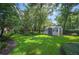 Spacious backyard featuring lush green lawn, mature trees, storage shed and meticulously landscaped flowerbeds at 511 Duque Rd, Lutz, FL 33549