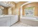 Well-lit bathroom boasts double sinks, soaking tub beneath arched window, and glass-enclosed shower at 5283 Bevens Ave, Spring Hill, FL 34608