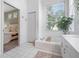 Bright bathroom featuring a soaking tub, white tiled floors, and a large window offering natural light at 2182 Trevor Rd, Palm Harbor, FL 34683
