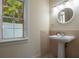 Elegant powder room featuring a pedestal sink, stylish mirror, and natural light from the window at 321 Barbara Cir, Belleair, FL 33756