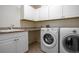Bright laundry room with granite counters, white cabinets, stainless steel sink, and modern, front-load washer and dryer at 321 Barbara Cir, Belleair, FL 33756
