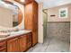 Well-lit bathroom featuring a wood vanity, round mirror, and tiled shower with glass door at 6505 Cedar Ne St, St Petersburg, FL 33702