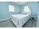 Light blue bedroom with white bed, matching side table, grey luxury vinyl flooring, and bright windows at 1317 S Betty Ln, Clearwater, FL 33756