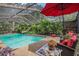Relaxing screened pool area with tropical landscaping and a bright red umbrella-shaded seating area at 7802 134Th St, Seminole, FL 33776