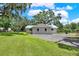 Rear side view of a home featuring green grass, mature trees and a gravel parking area at 9448 Mcintyre Rd, Brooksville, FL 34601