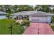 Single-Gathering home featuring a red brick driveway, mature landscaping, and an attached garage, providing comfortable living at 1607 New Bedford Dr, Sun City Center, FL 33573